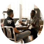 two men talking, seated at a table