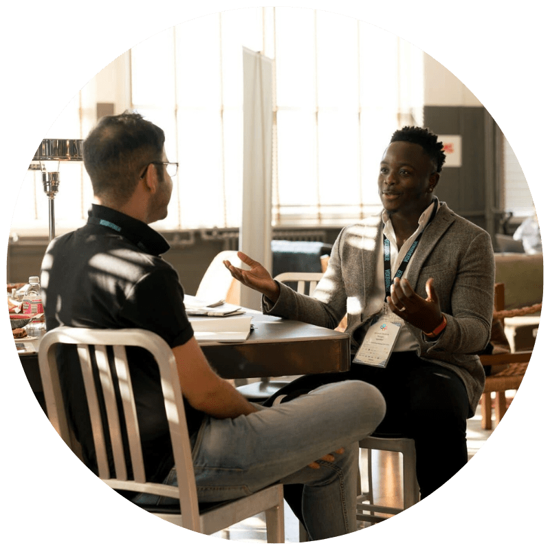 two men talking, seated at a table